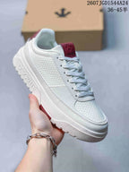 Close side view of a white DESCENTE Dualis sneaker with red tongue accent and textured upper panel.