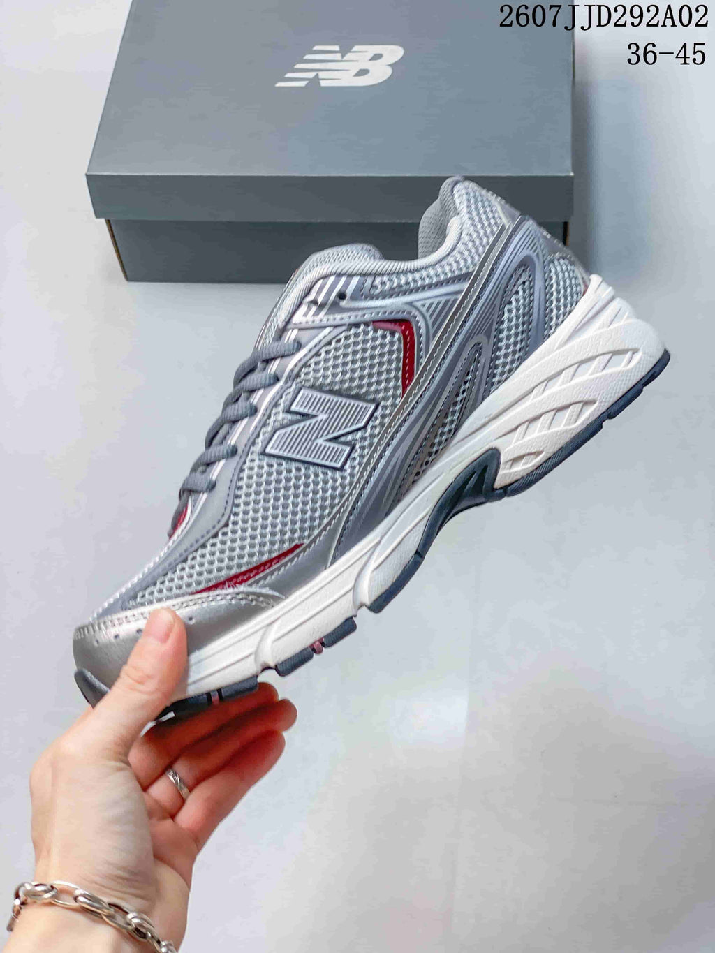 Side profile of a gray, white, and red New Balance 509 sneaker with layered panels, large N logo, white midsole, and dark outsole.