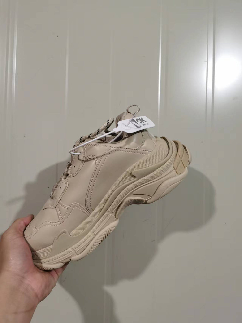 Rear and lateral view of the beige Balenciaga Triple S sneaker showing the heel construction, layered sole, and hanging product tag.