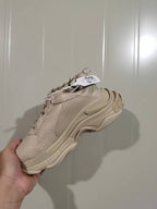Rear and lateral view of the beige Balenciaga Triple S sneaker showing the heel construction, layered sole, and hanging product tag.