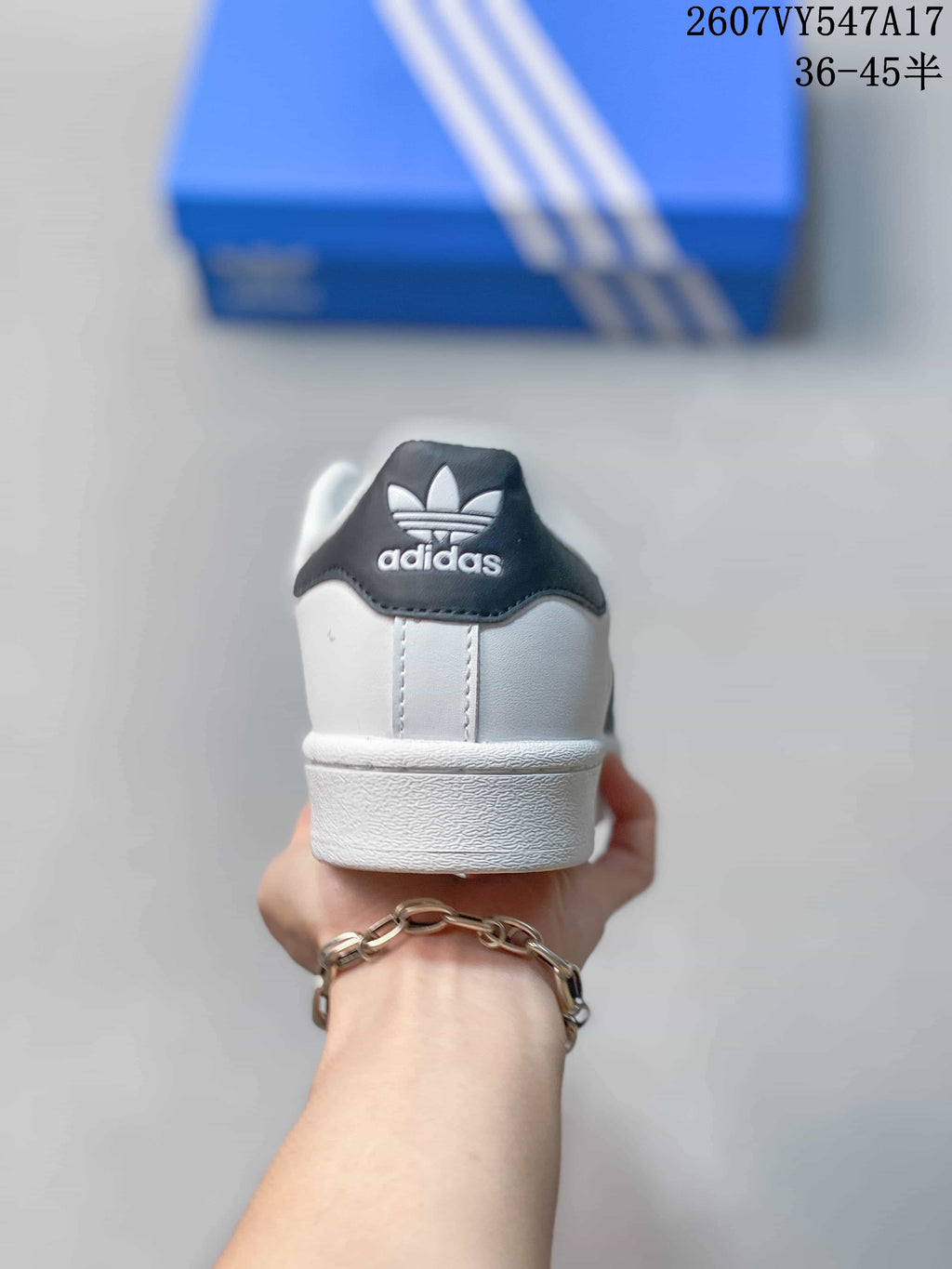 Rear view of a white sneaker showing a black heel panel, Adidas trefoil branding, and a white textured midsole.