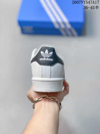 Rear view of a white sneaker showing a black heel panel, Adidas trefoil branding, and a white textured midsole.