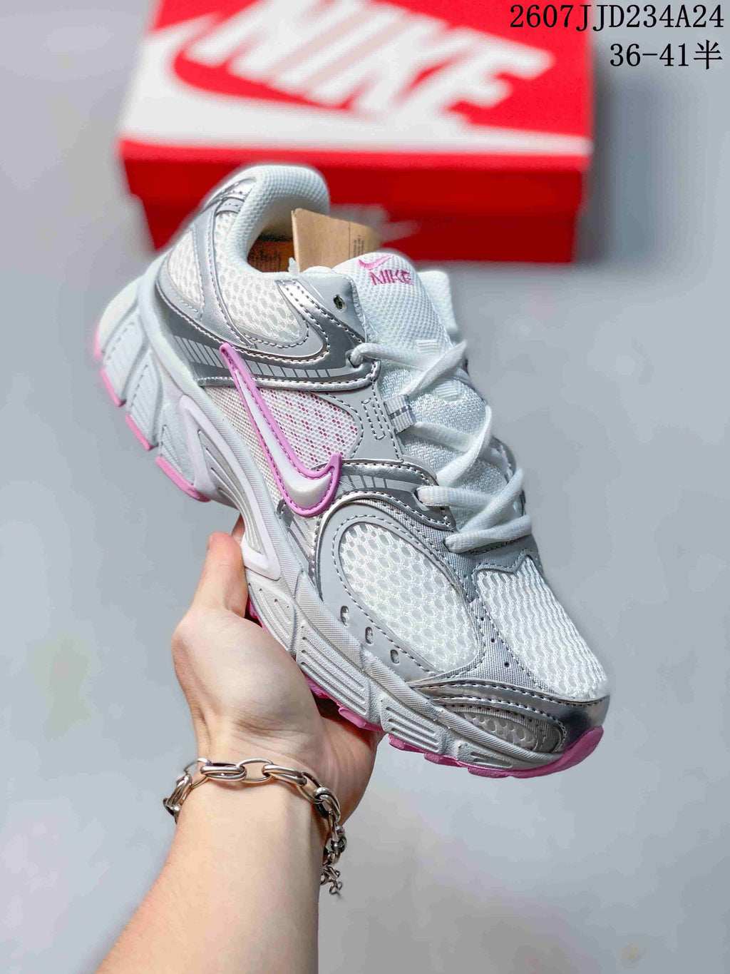 Angled side view of a white, silver, and pink Nike sneaker with layered overlays and a textured sole; overlay shows style code 2607JJD234A24 and sizes 36–41.5.