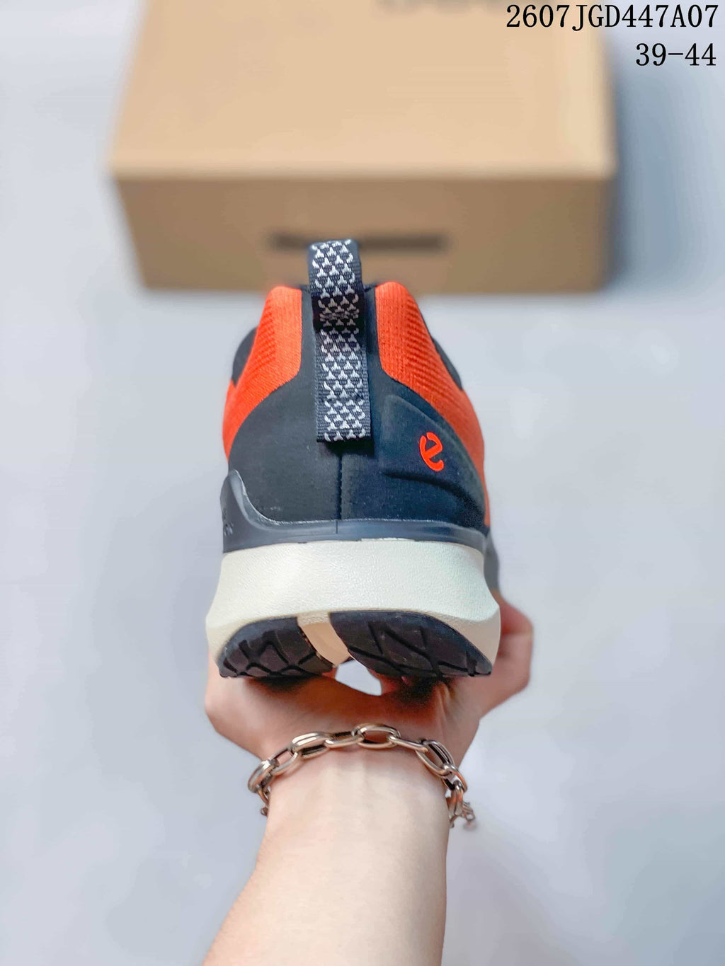 Rear view of an orange and navy ECCO sneaker showing the heel pull tab, dark heel panel, and light midsole.