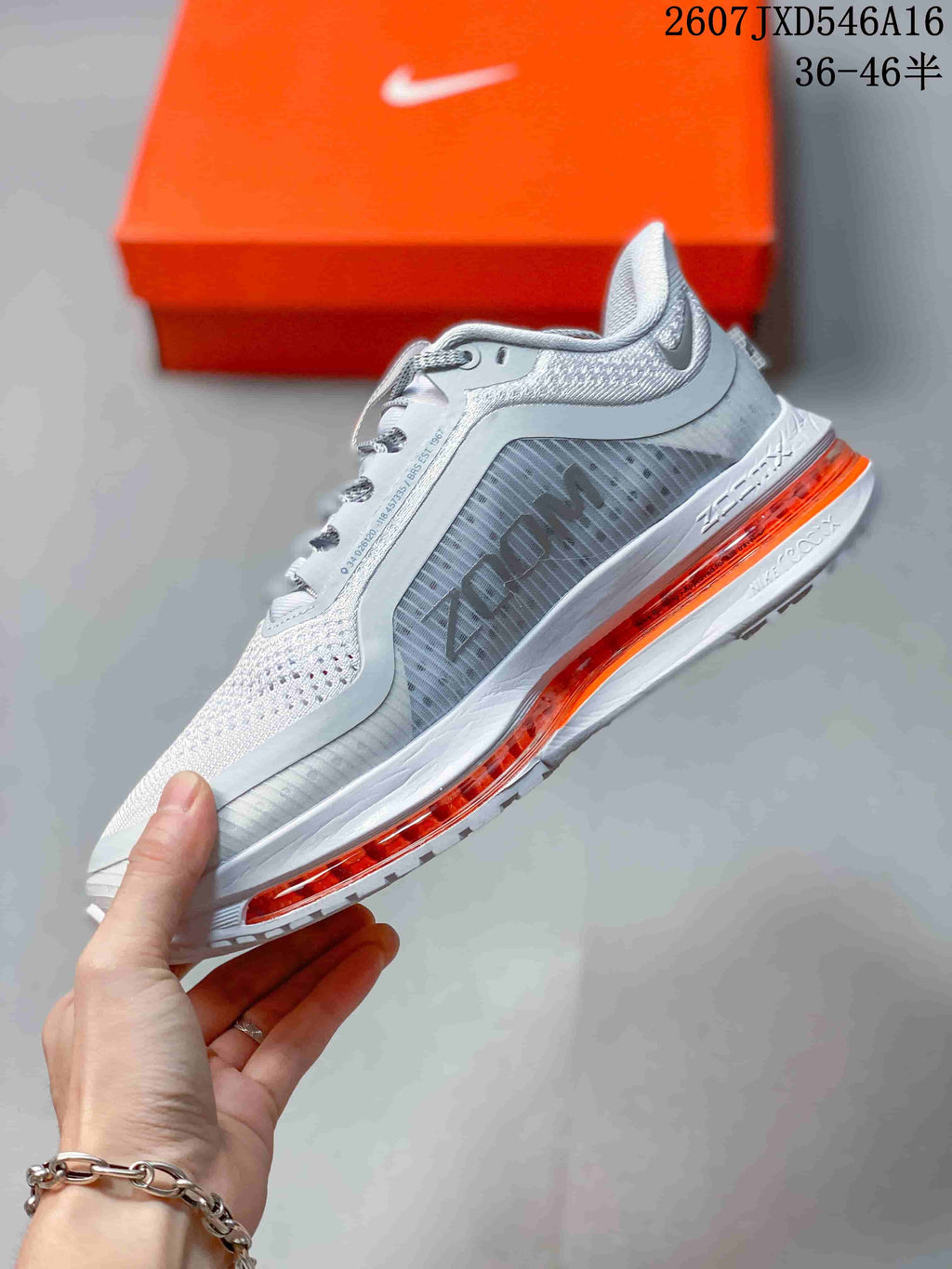 Side view of the white and gray sneaker showing the perforated upper, Nike branding, layered panels, and orange midsole element.