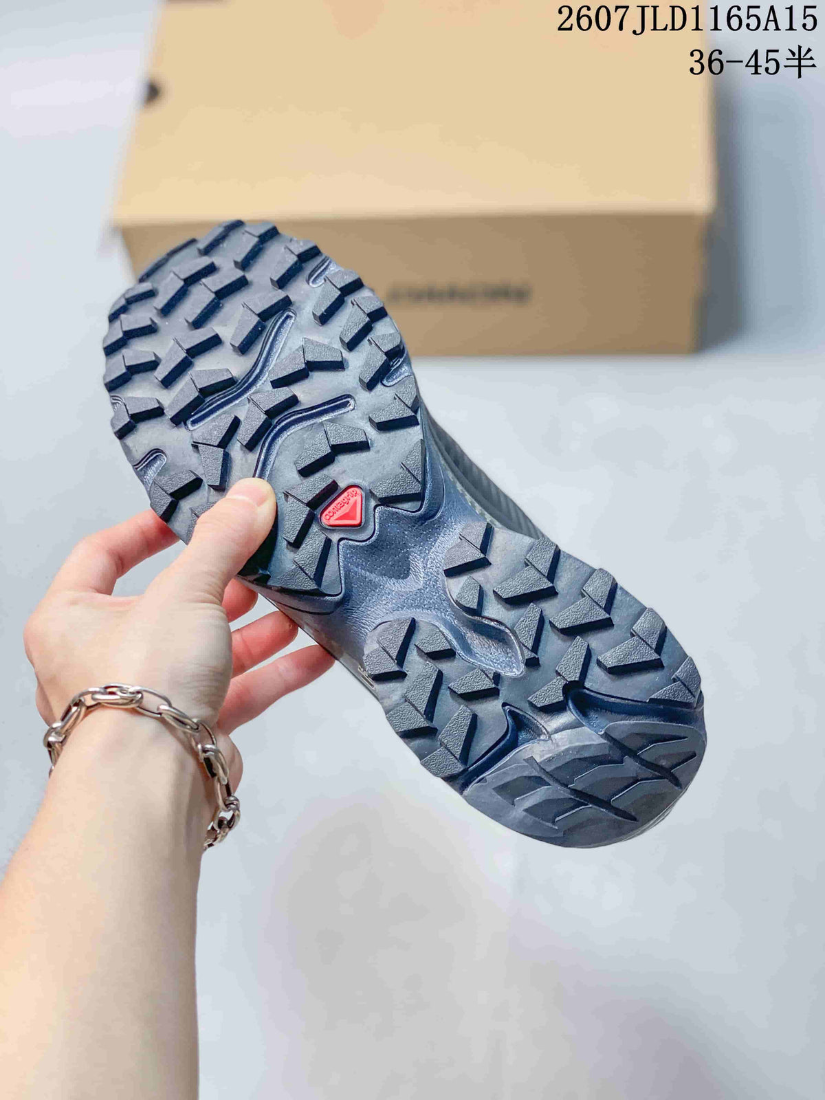 Close view of the black sneaker outsole, showing its deep lugged tread pattern and red Salomon detail.