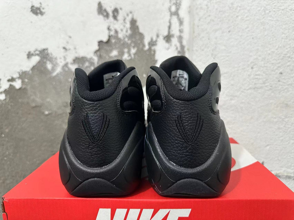 Rear view of a pair of black Nike sneakers showing heel panels and embroidered details.