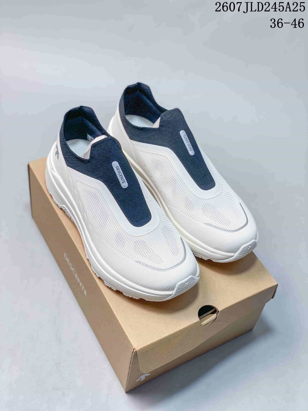 Pair of white and navy DESCENTE slip-on sneakers shown on a shoebox, with the style code and size range visible above.