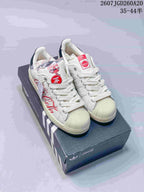Pair of white Adidas Superstar sneakers with Coca-Cola graphics displayed on a branded shoe box.