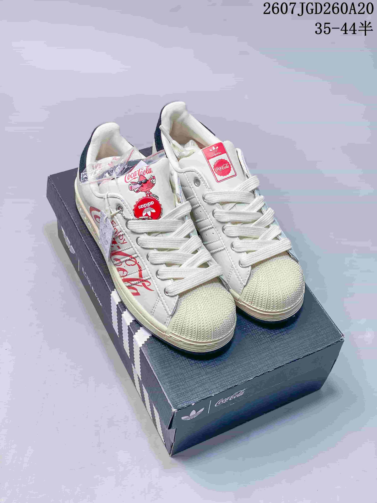 Pair of white Adidas Superstar sneakers with Coca-Cola graphics displayed on a branded shoe box.