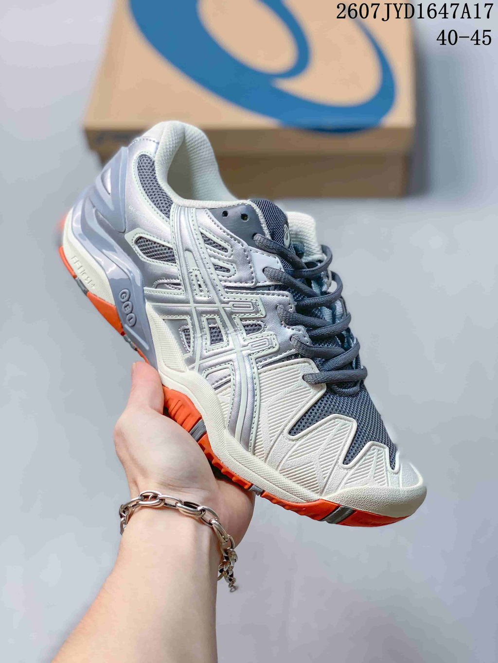 White and gray ASICS GEL-Resolution 5 tennis shoe with orange outsole accents; image text shows style code 2607JYD1647A17 and size range 40–45.