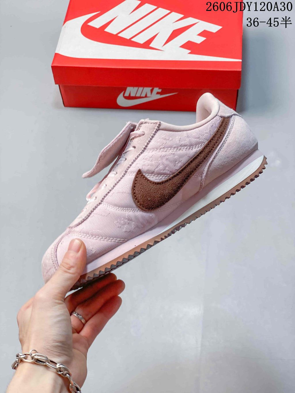Side view of a pale pink Nike Classic Cortez sneaker with a brown side logo