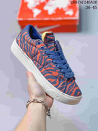 Angled side view of the blue and orange low-top sneaker with white outsole and decorative midsole detailing.