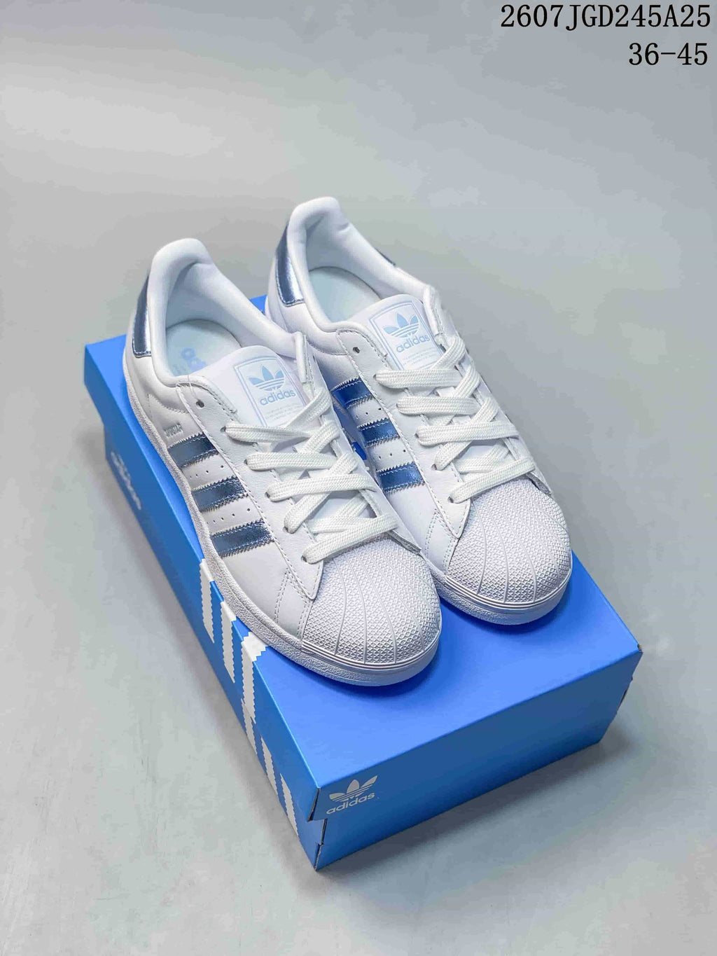 Pair of white and blue adidas Superstar sneakers displayed on a blue shoebox.