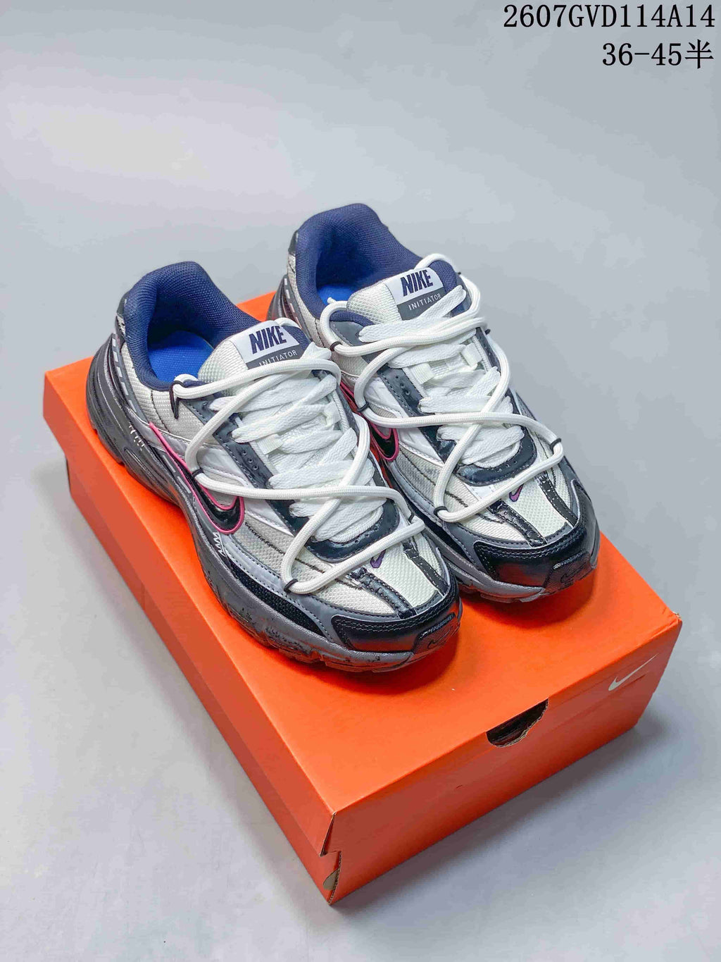 Pair of gray, white, and black Nike Initiator RNR sneakers displayed on an orange shoebox.