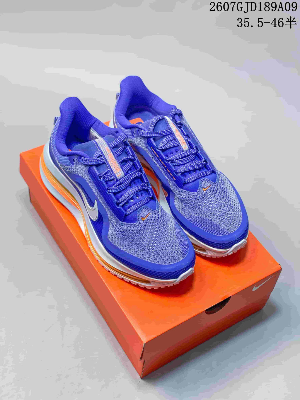 Pair of blue Nike Vomero Premium running shoes displayed on an orange Nike shoe box, with the source size range and style code visible above.