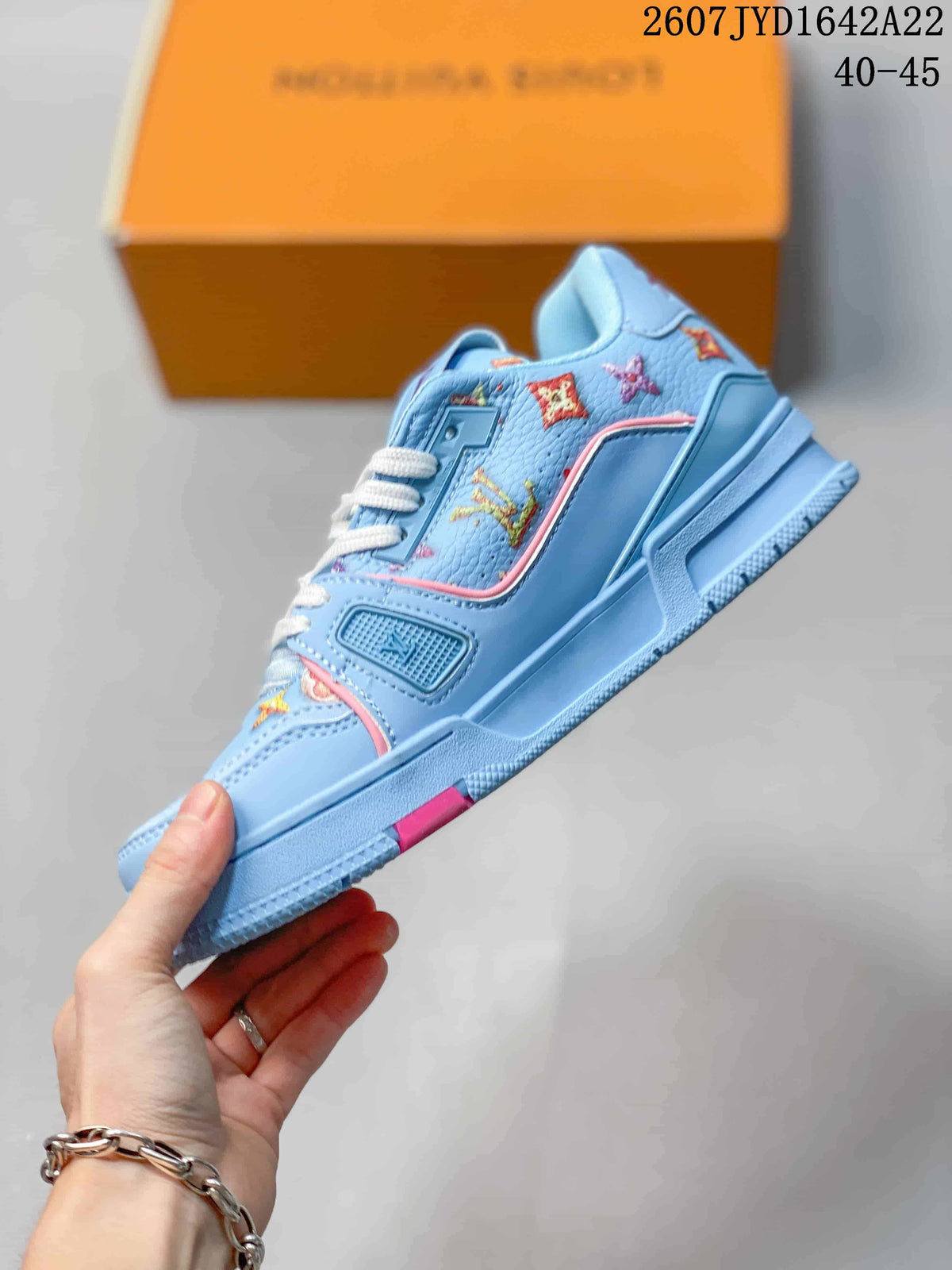 Side profile of a light blue low-top sneaker with pink trim, multicolor patterned upper panels, and a textured sole.