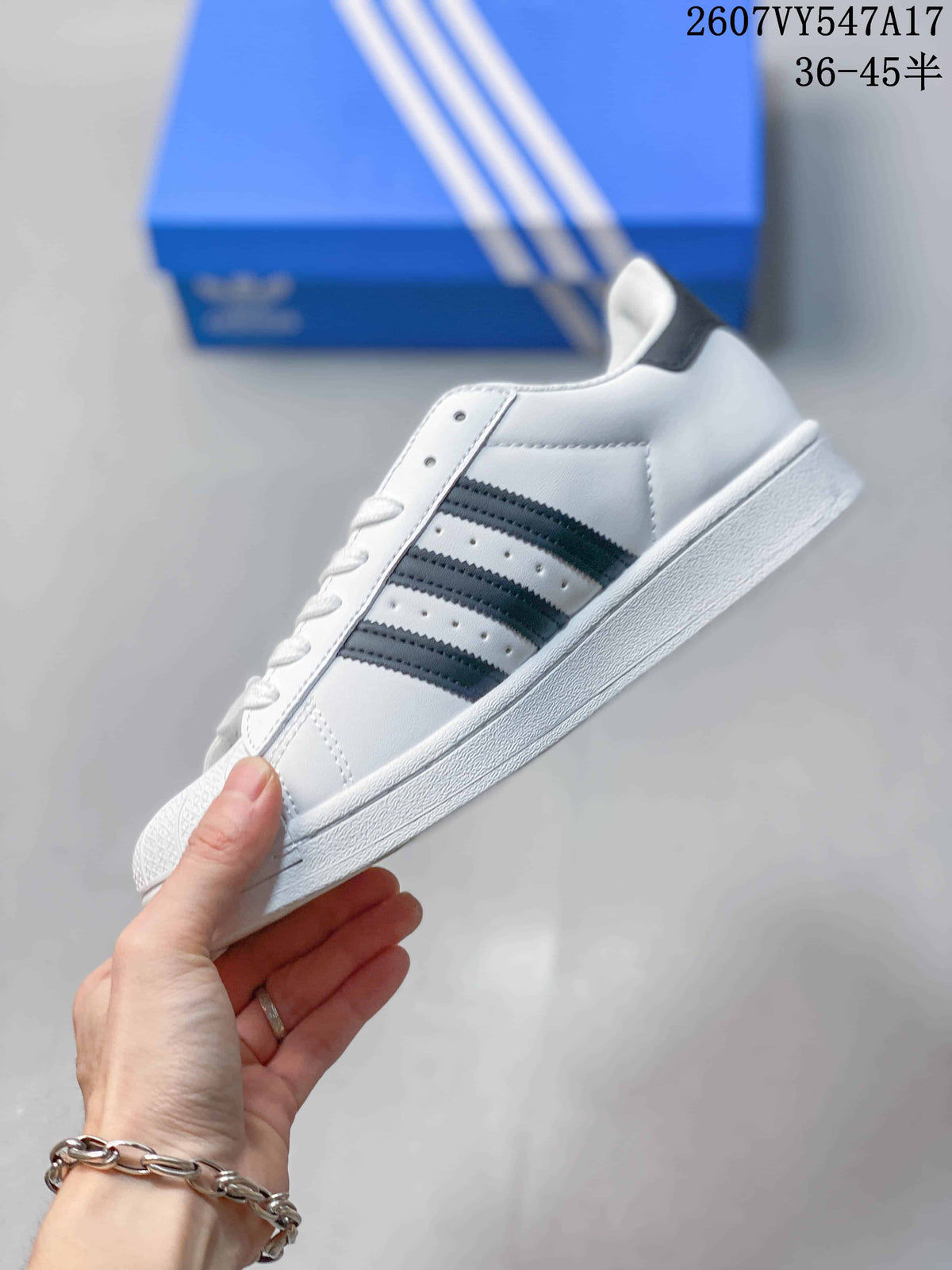 Side view of a white Adidas Superstar sneaker with black three-stripe detailing and a white rubber sole.