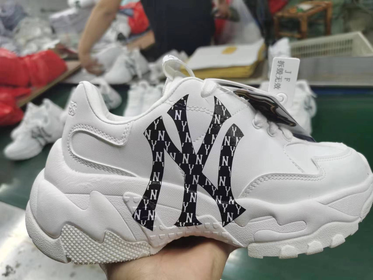 White chunky MLB sneaker with black monogram-style lettering panels, padded collar, white laces, and a sculpted textured sole.