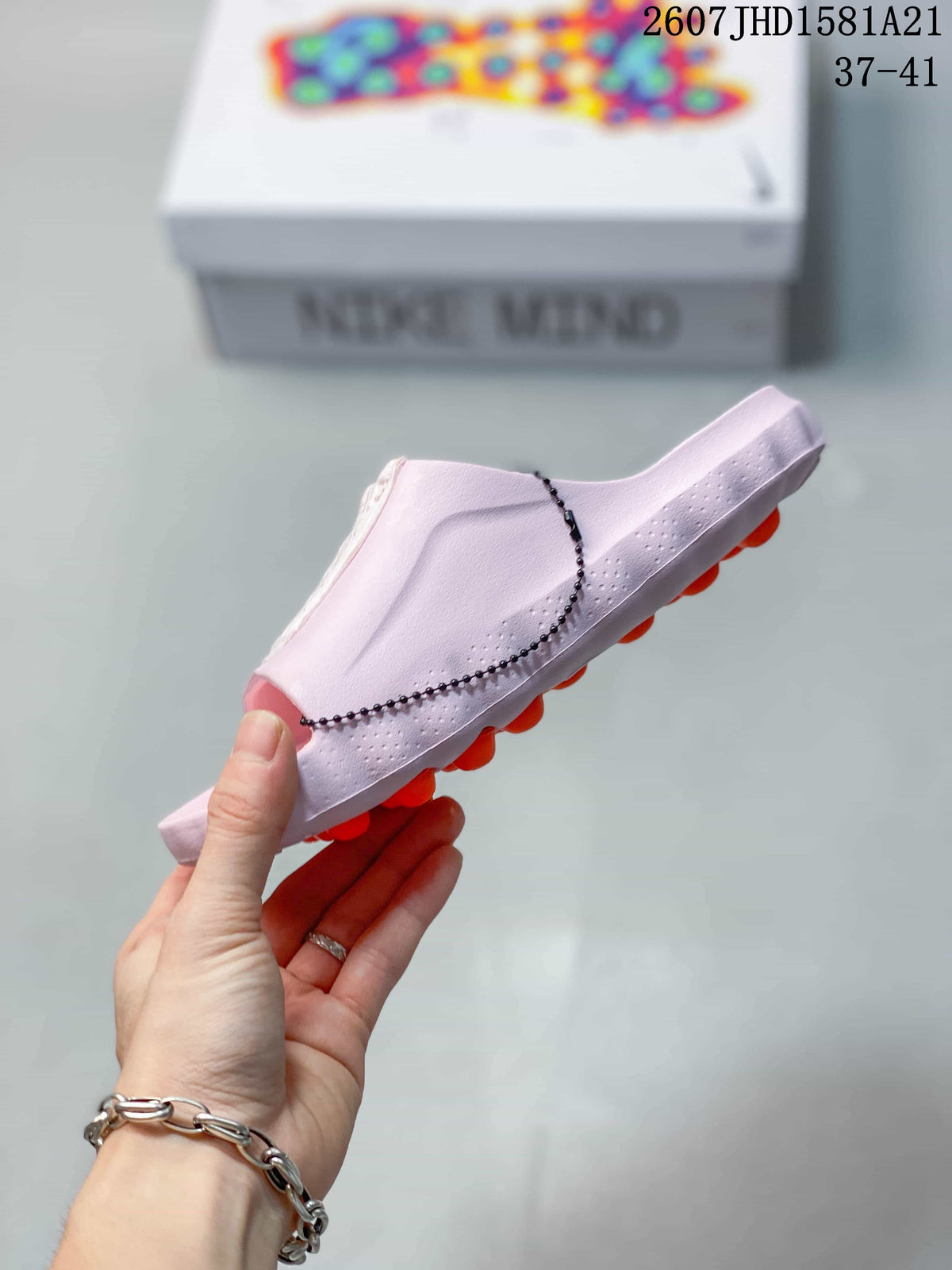 Side profile of the light pink mule slide showing its wide upper, textured sole edge and orange outsole pods.