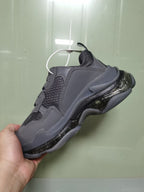 Rear three-quarter view of the dark grey sneaker showing the padded collar, mesh heel area, layered panels and glossy black sole details.