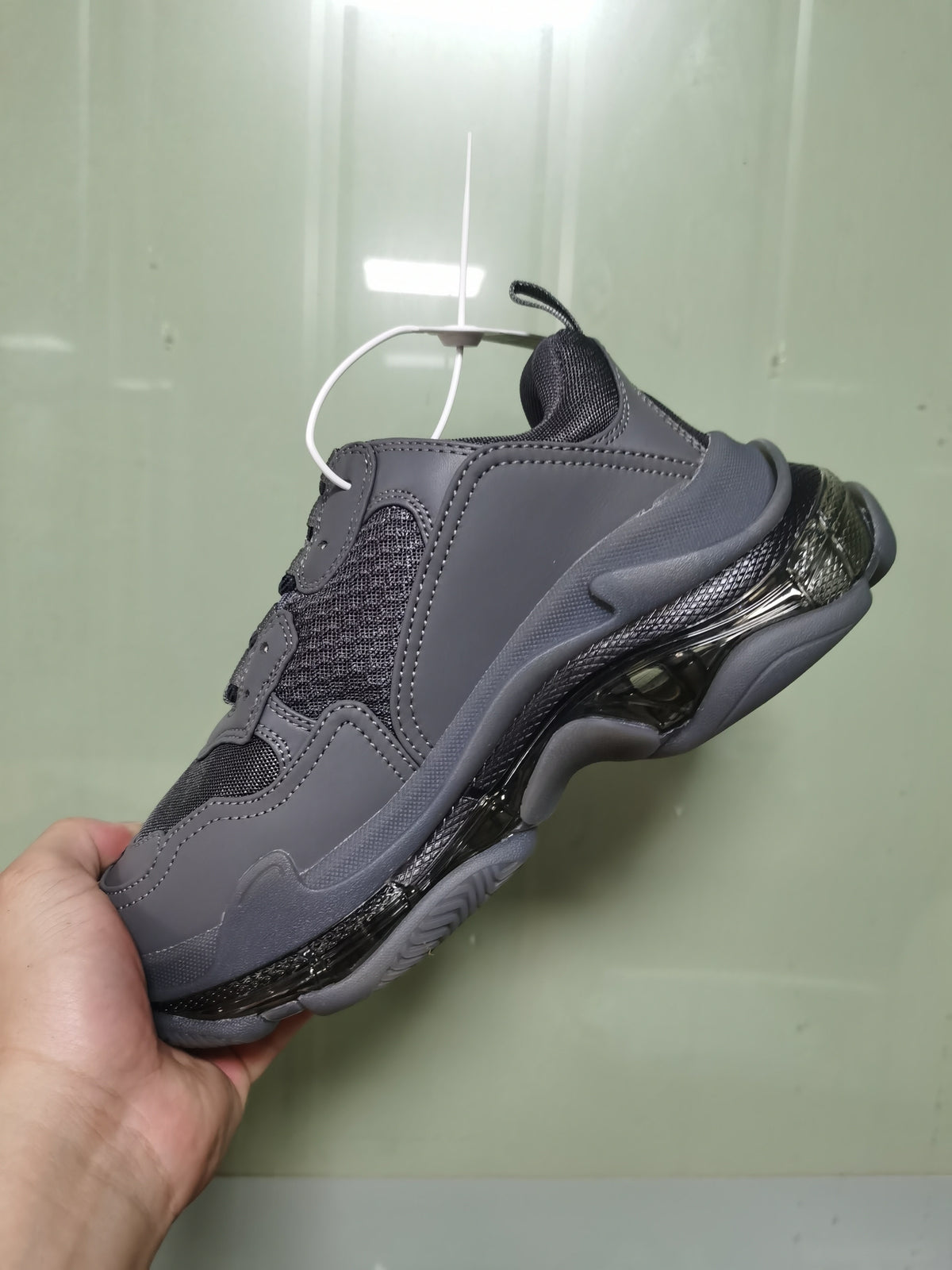 Rear three-quarter view of the dark grey sneaker showing the padded collar, mesh heel area, layered panels and glossy black sole details.