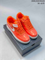 Pair of bright orange low-top sneakers with white Swoosh and sole, displayed on a dark box.
