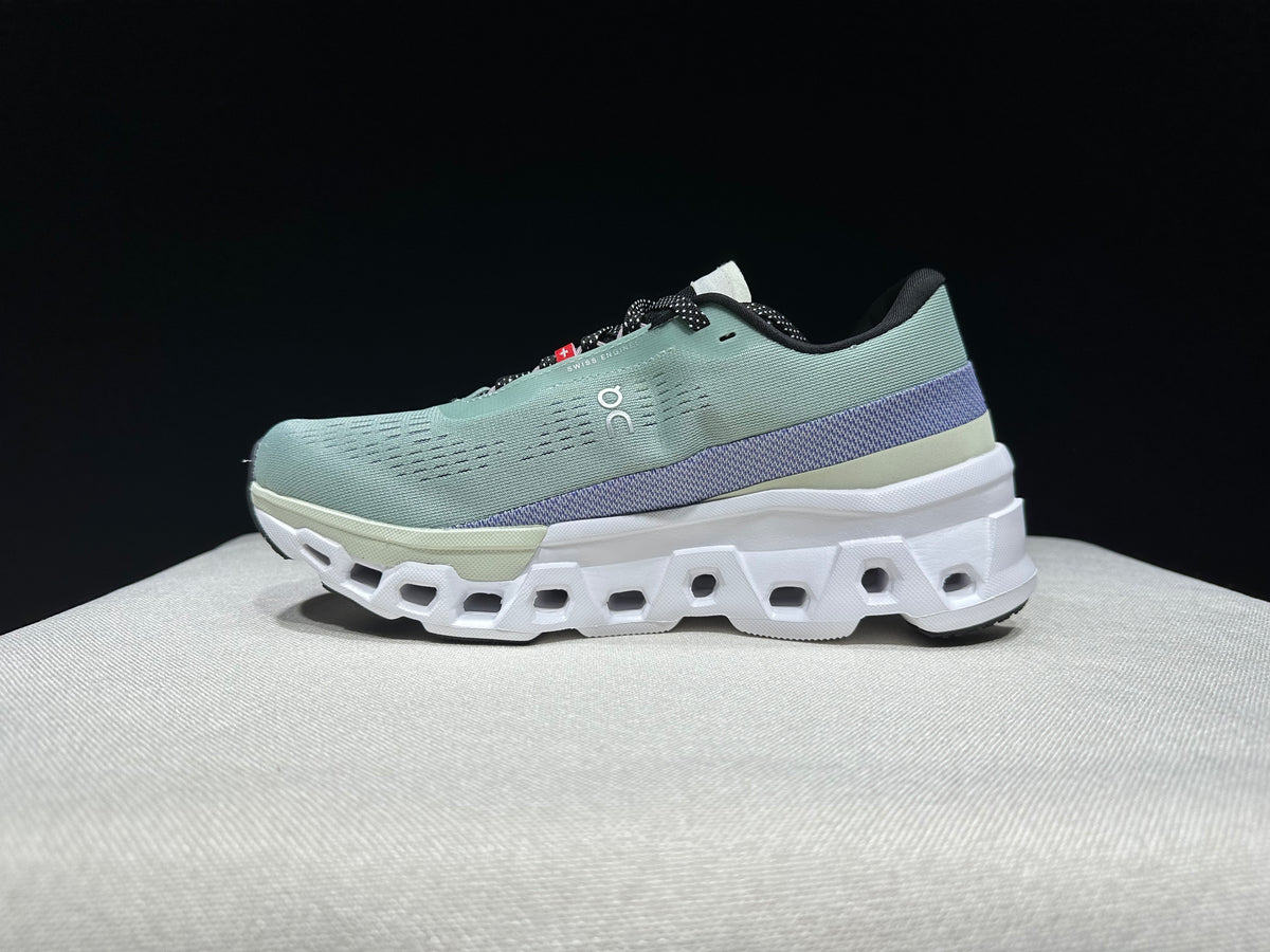 Side view of a pale green On Cloudmonster 2 shoe with purple heel detailing and a sculpted white sole.