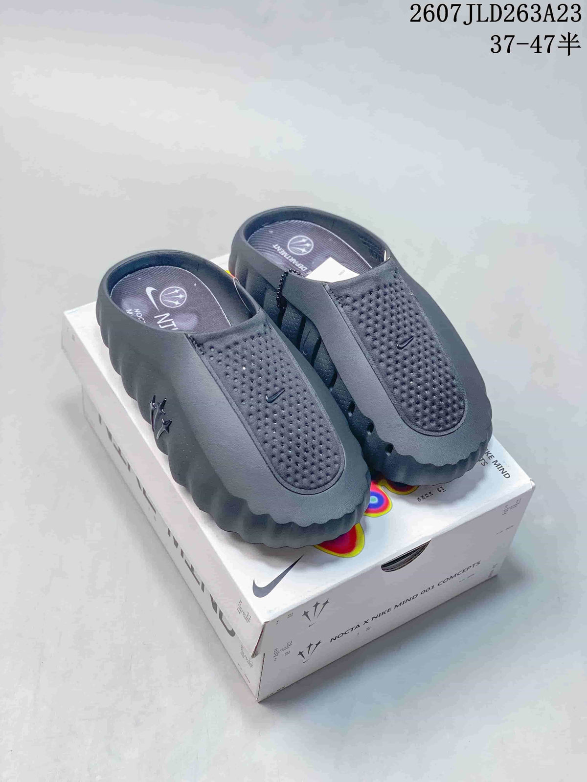 Black Nike Mind 001 slides displayed on a box, showing the slip-on shape, perforated upper and deeply textured sole.
