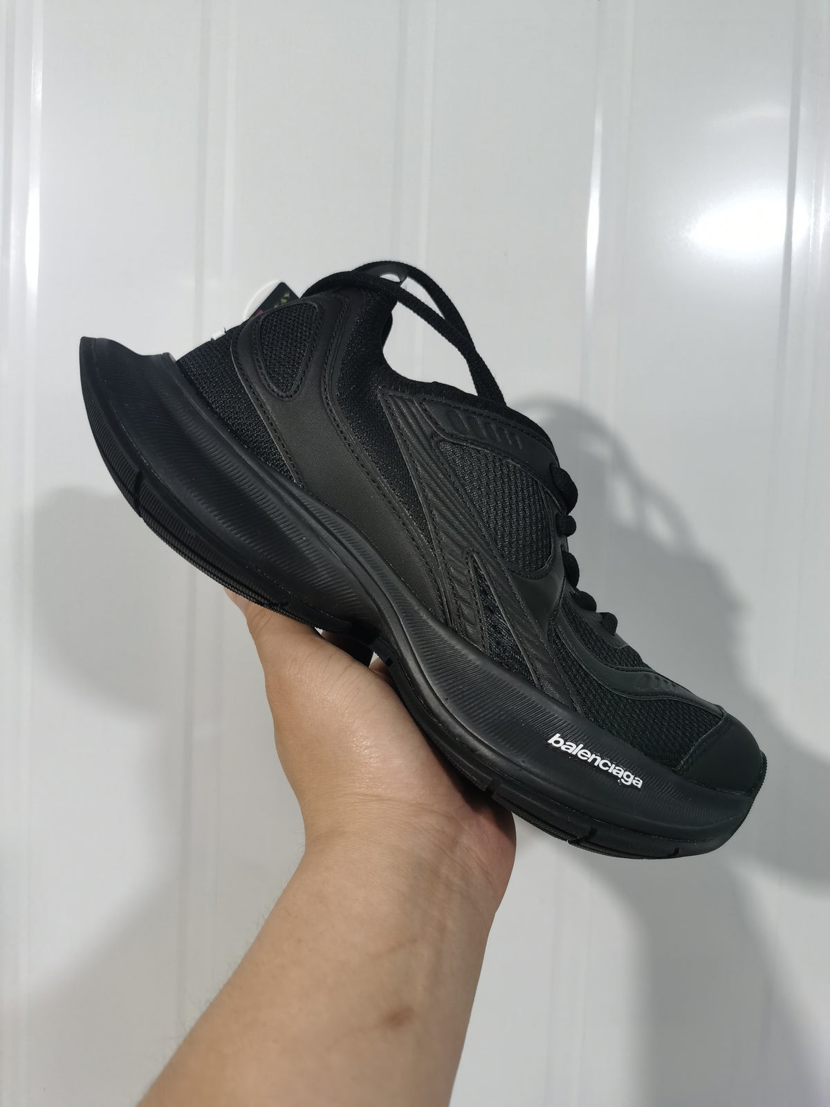 Side view of a black Balenciaga Circuit sneaker held in hand, with Balenciaga branding visible on the sole.