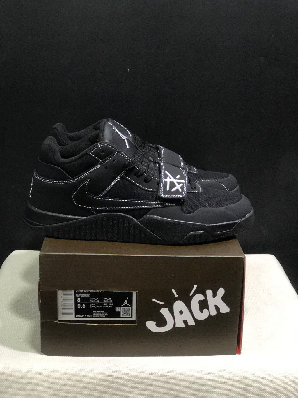 Side view of black Jordan Jumpman Jack sneakers showing white contrast stitching, lateral Swoosh and forefoot straps.