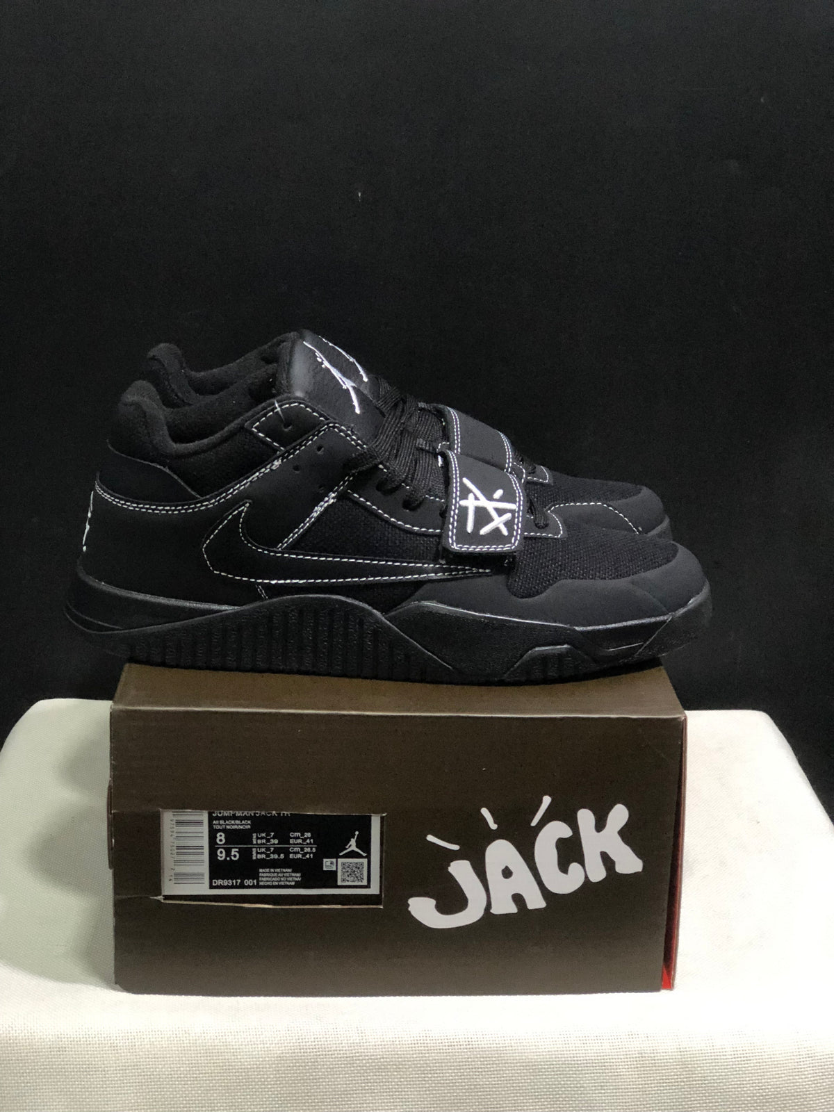 Side view of black Jordan Jumpman Jack sneakers showing white contrast stitching, lateral Swoosh and forefoot straps.