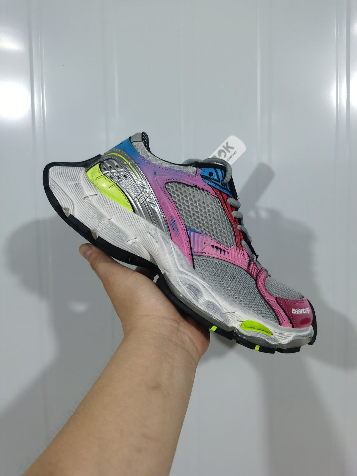 Side view of a multicolor sneaker showing gray mesh panels, pink and blue overlays, metallic silver detailing, neon yellow accents, and a sculpted white midsole.