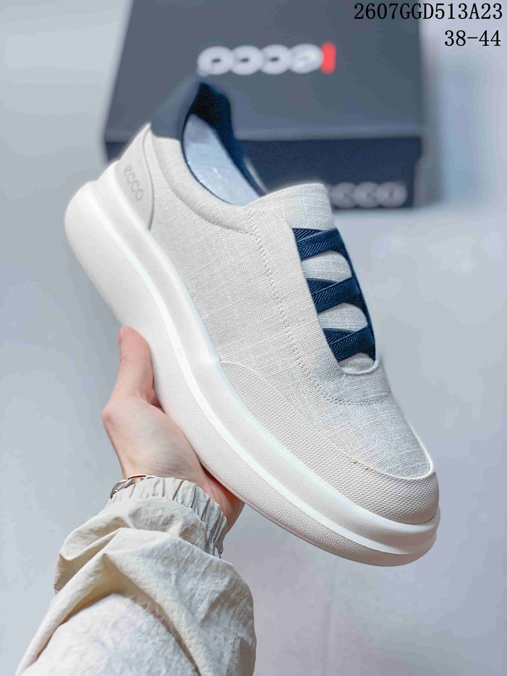 Angled side view of the light gray sneaker showing the navy crossover bands, heel branding, and raised white outsole.