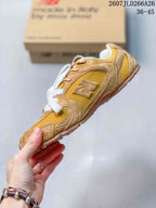 Side profile of the mustard and tan low-top sneaker showing the stitched New Balance logo and layered panels.