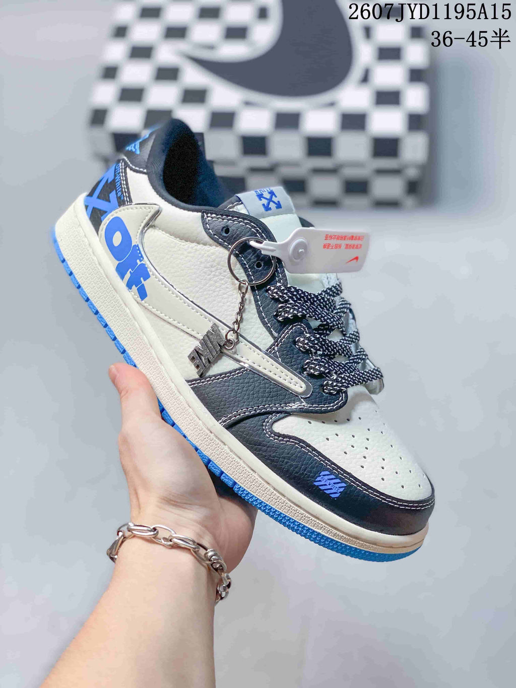 Side view of a white, black and blue low-top sneaker showing layered overlays, patterned laces, a decorative hangtag and blue outsole.