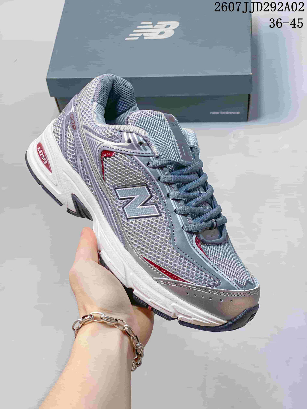 Angled close view of a gray, white, and red New Balance 509 sneaker showing the large N logo, lace-up closure, layered upper, and outsole.