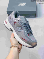 Angled close view of a gray, white, and red New Balance 509 sneaker showing the large N logo, lace-up closure, layered upper, and outsole.