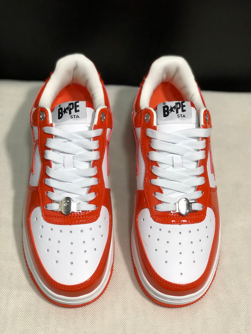 Front top view of the pair showing the white toe boxes, orange trim, laces, and BAPE Sta tongue branding.