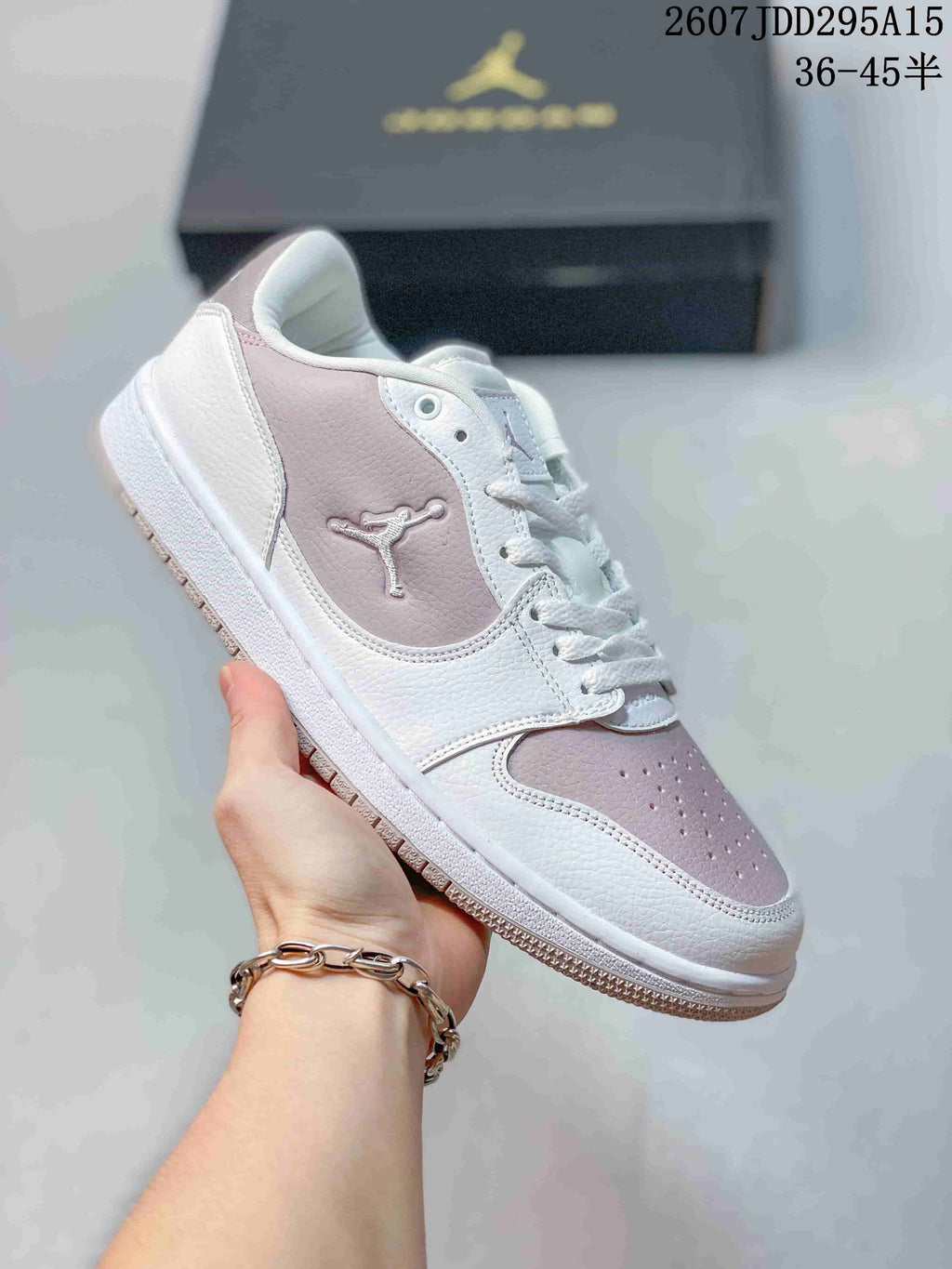 White and pale pink low-top Jordan sneaker held at an angle, with pink heel and toe panels and a pale outsole accent.