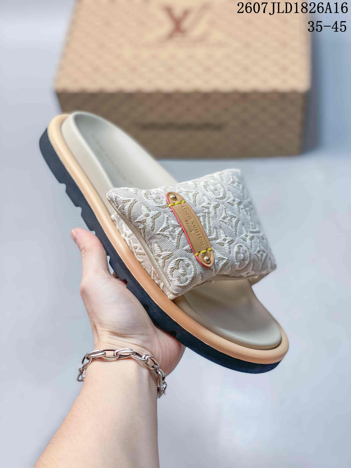 Angled close view of the slide sandal showing the monogram-patterned strap, decorative plaque, light footbed, and dark outsole.
