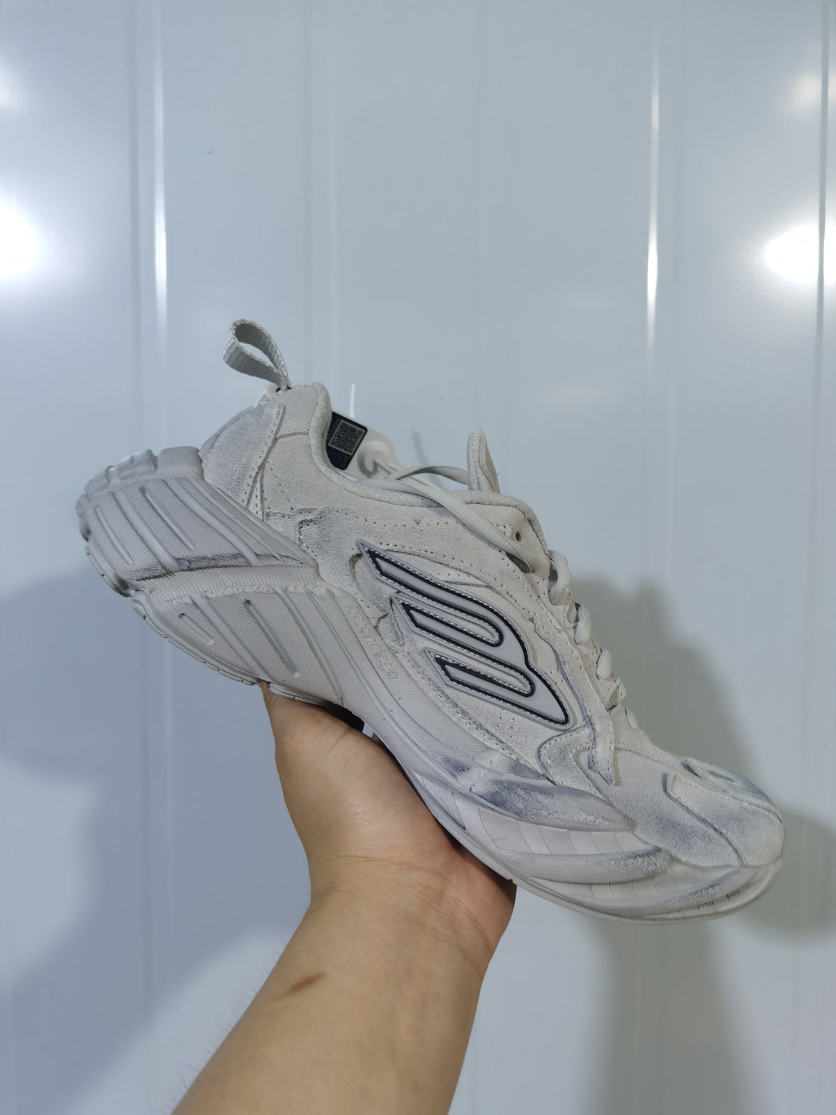 Angled side view of the beige New Balance 9090 sneaker showing layered panels, outlined side branding, and the sculpted outsole.