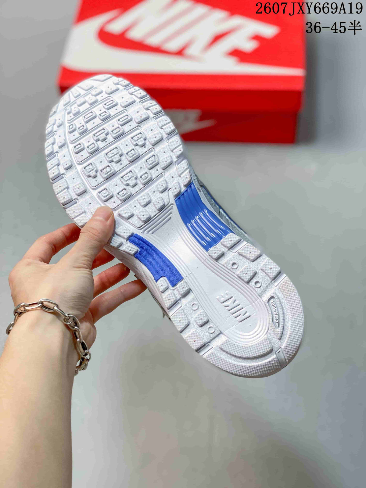 Close-up of the patterned white outsole with blue accent sections, held above a red Nike shoebox.