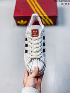 Top view showing white laces, a shell toe, and a red tongue label with gold-colored branding.