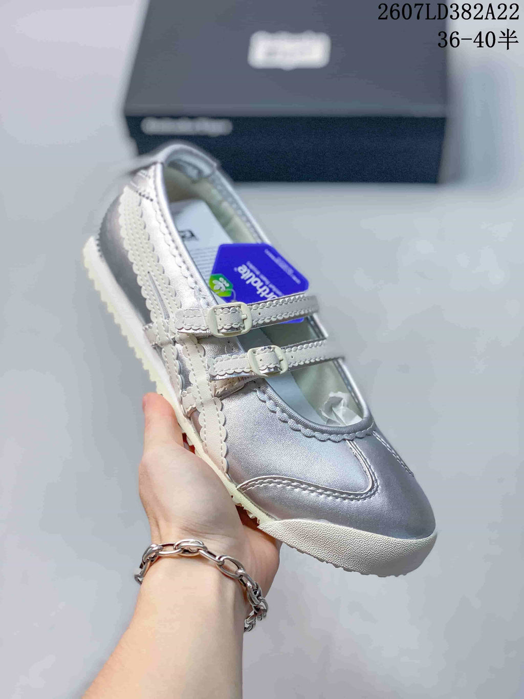 Close view of a silver shoe showing its twin buckle straps, scalloped side stripes, and textured outsole.
