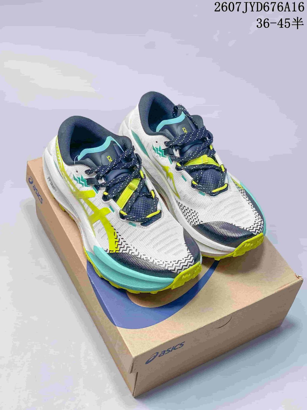 Pair of white ASICS trail running shoes with navy, lime, and turquoise details displayed on an ASICS shoebox; image text shows style code 2607JYD676A16 and size range 36–45.