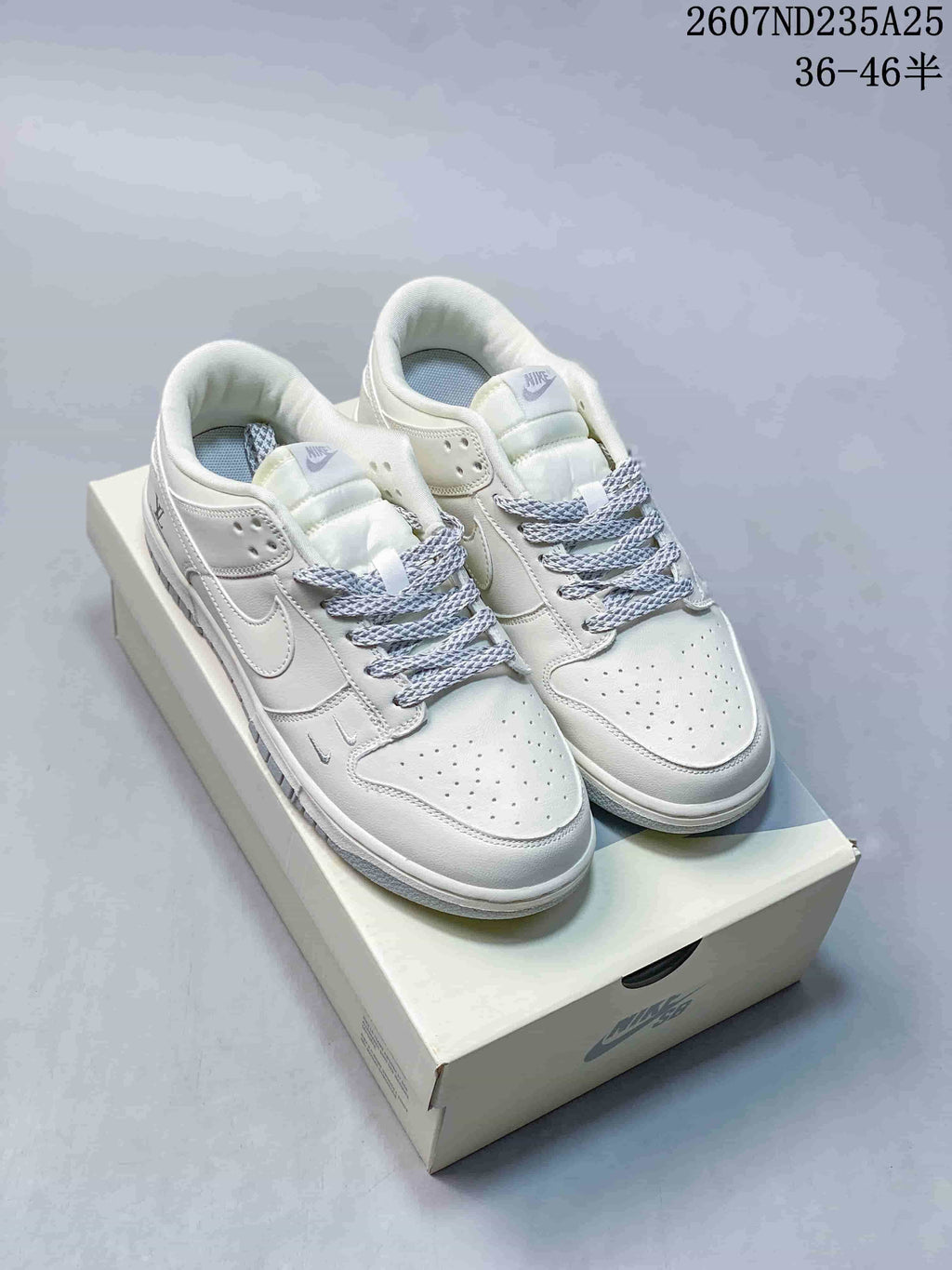 Pair of white low-top sneakers with grey patterned laces, perforated toe panels and textured outsole tread.