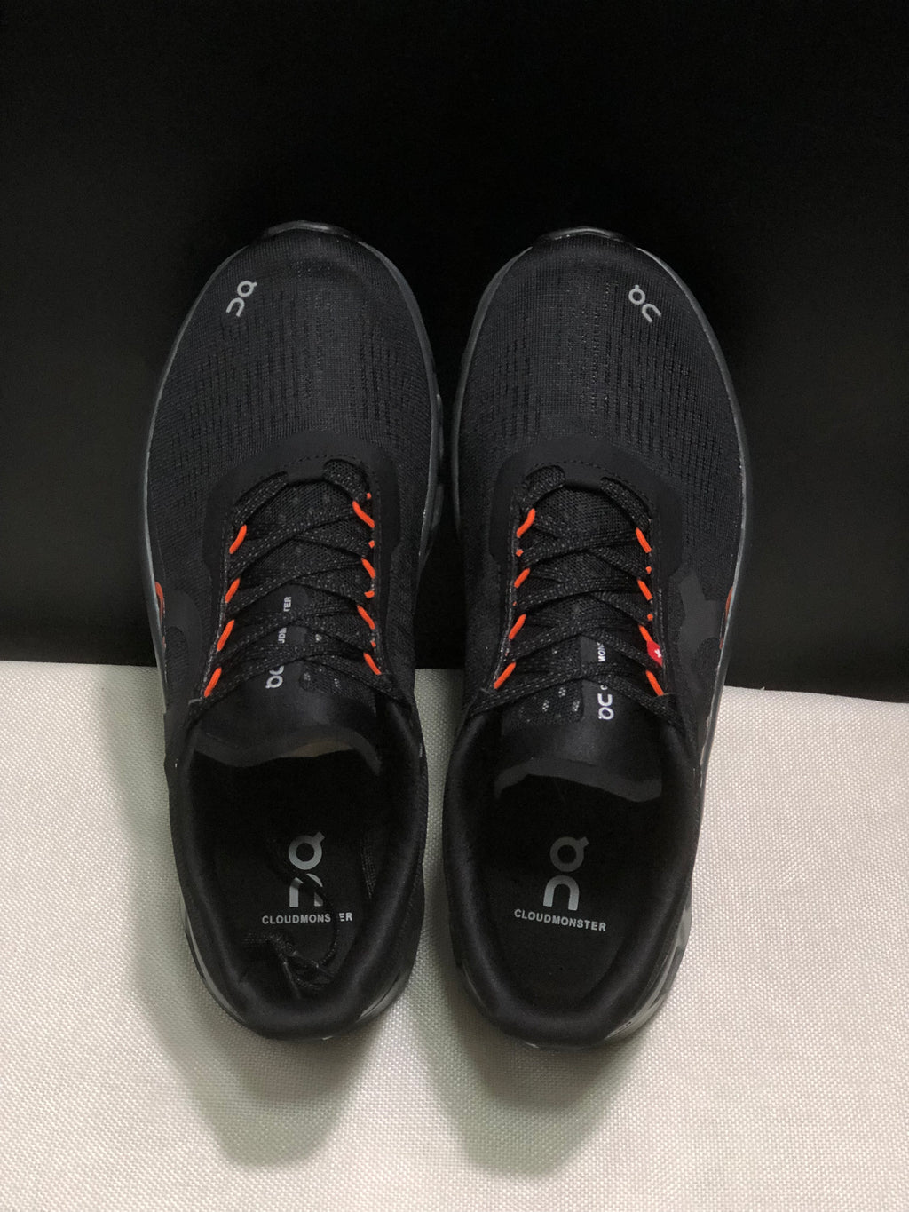 Top-down view showing the black uppers, lace system, orange lace accents, and branded insoles.