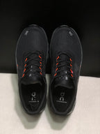 Top-down view showing the black uppers, lace system, orange lace accents, and branded insoles.