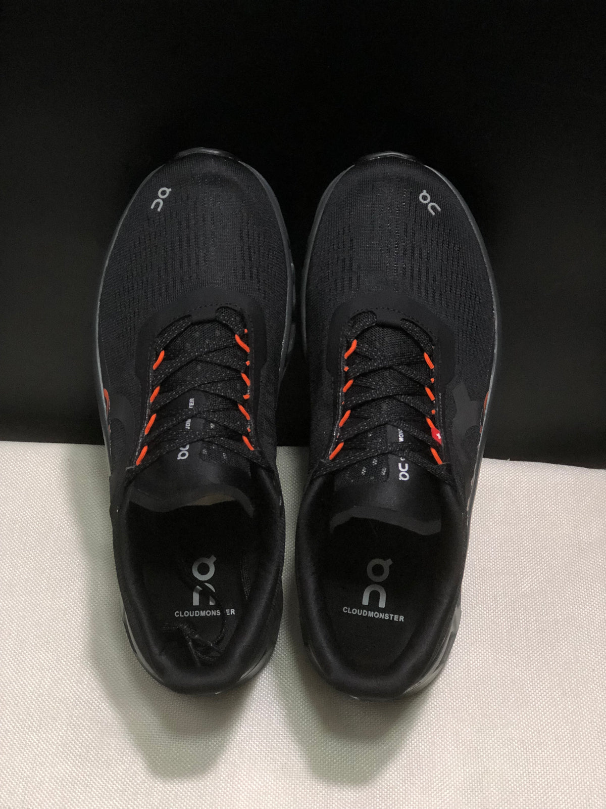 Top-down view showing the black uppers, lace system, orange lace accents, and branded insoles.